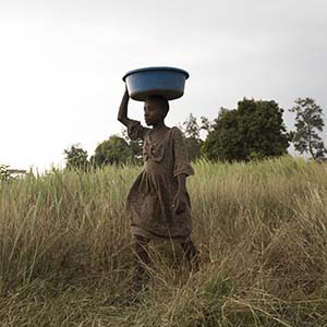 A girl carries a bucket of animal food over her head.